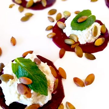 Three Marinated Beet Bites with feta and mint garnished with toasty pumpkin seeds on white background