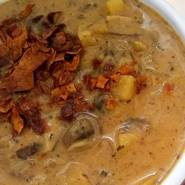 Close up view of New England Vegan Clam Chowder garnished with zucchini bacon, in a white bowl