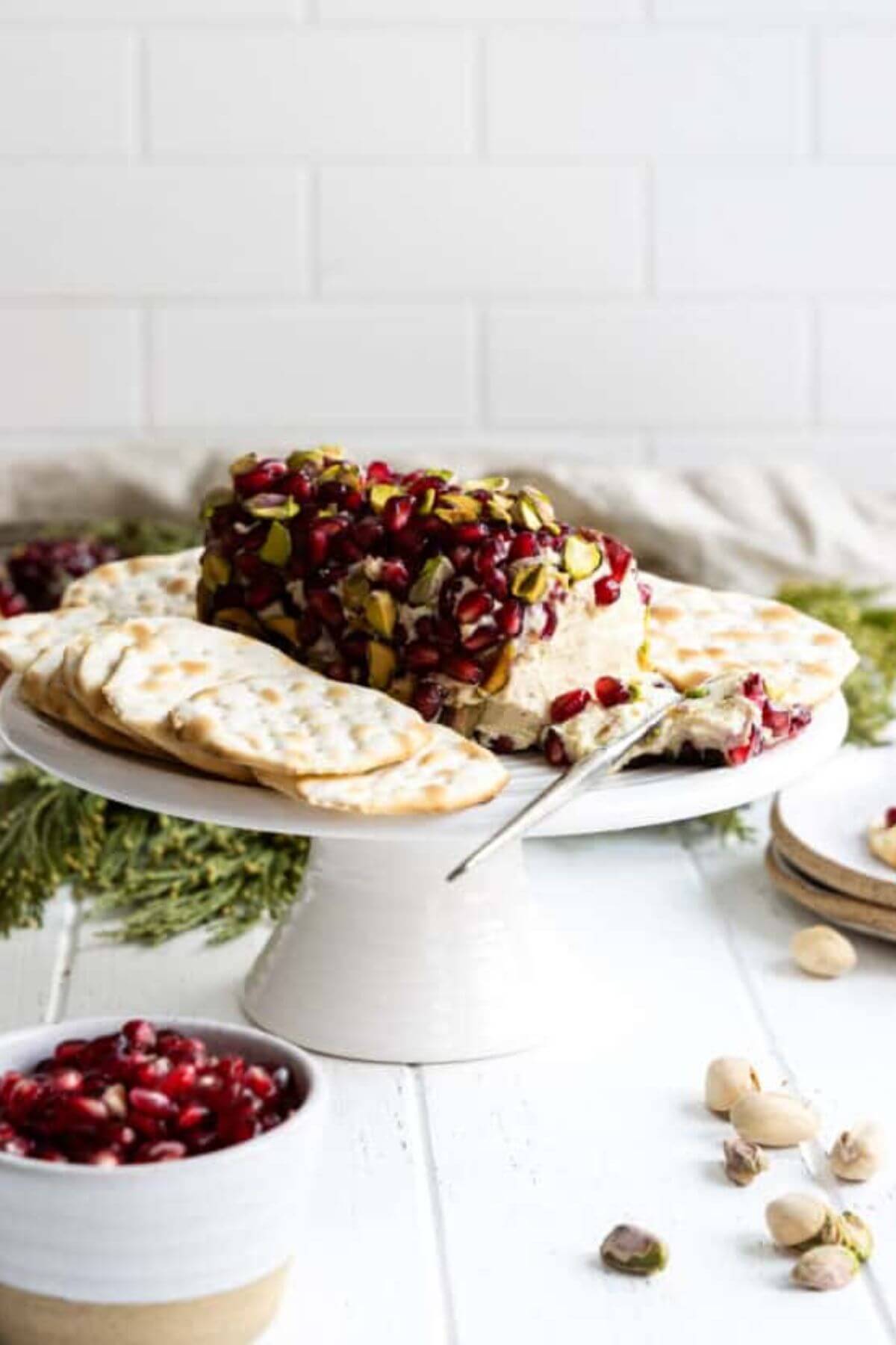 Pomegranate-Pistachio-Cheese-Log on a pedistal with a bowl of pomegranates and pistachios on the side